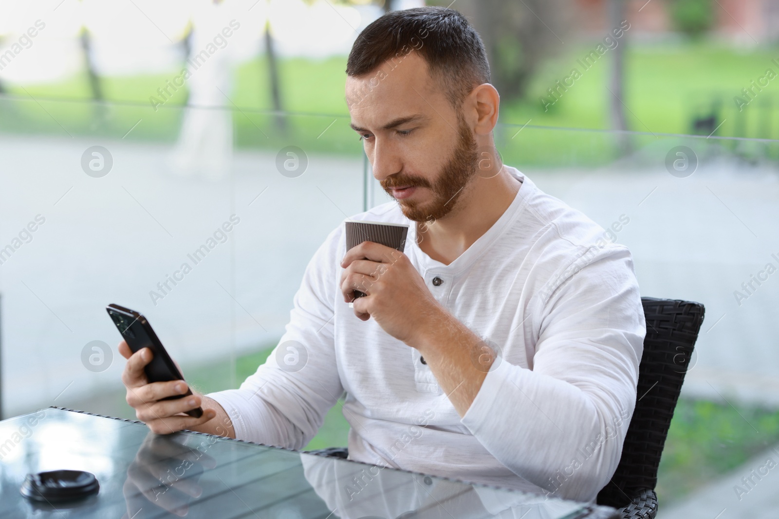 Photo of Handsome man using smartphone and drinking coffee at outdoor cafe