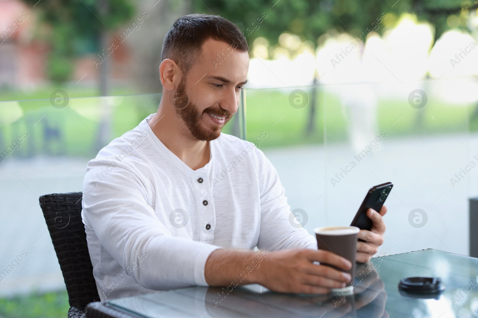 Photo of Happy man using smartphone and drinking coffee at outdoor cafe