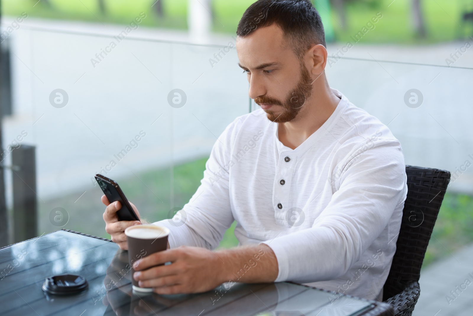 Photo of Handsome man using smartphone and drinking coffee at outdoor cafe