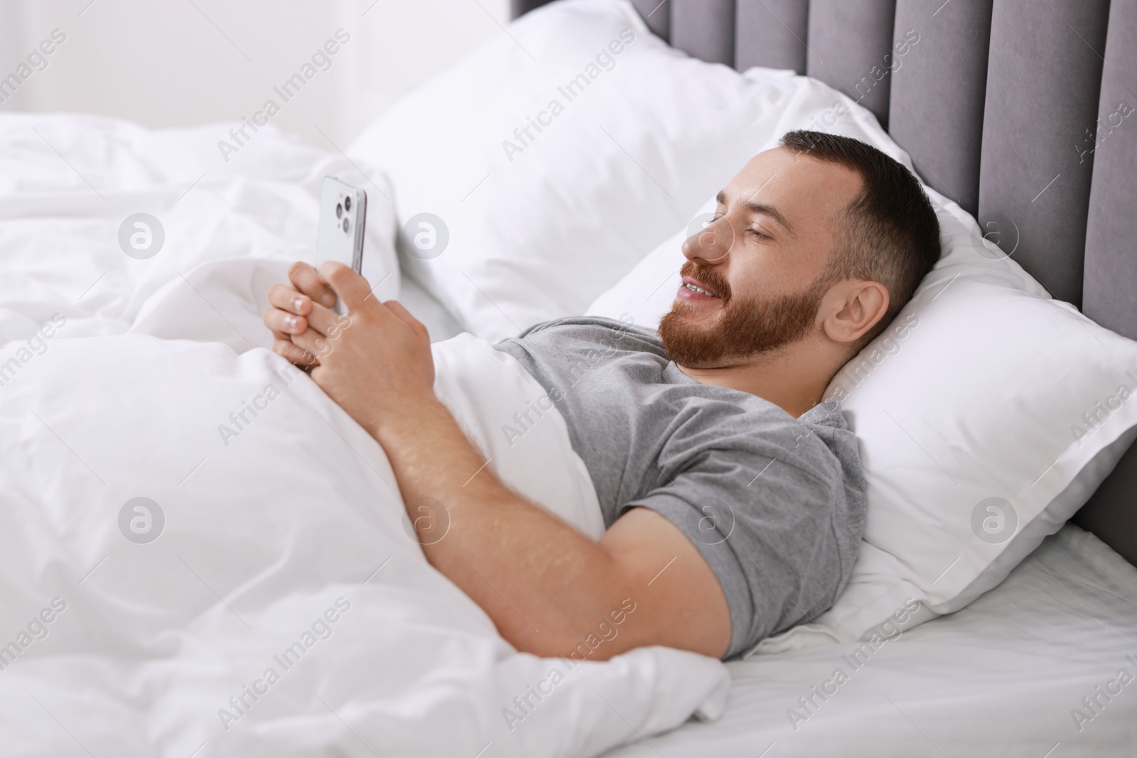 Photo of Smiling man using mobile phone in bed