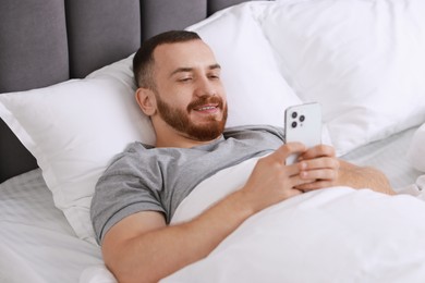 Photo of Smiling man using mobile phone in bed