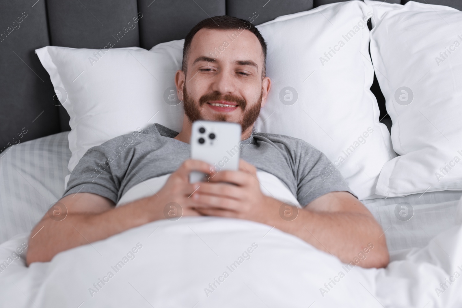 Photo of Smiling man using mobile phone in bed