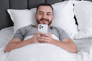 Smiling man using mobile phone in bed