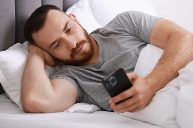 Handsome man using mobile phone in bed