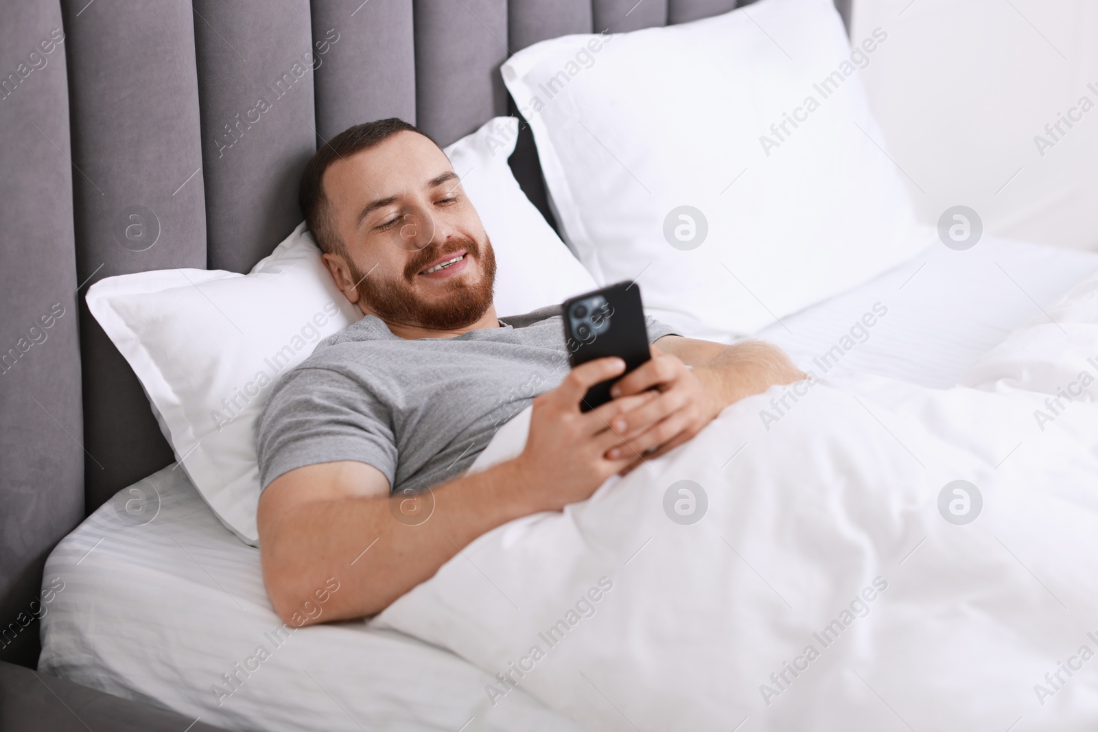 Photo of Smiling man using mobile phone in bed