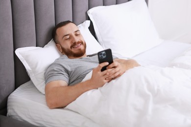 Photo of Smiling man using mobile phone in bed