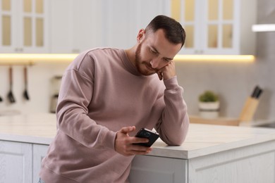 Handsome man looking at smartphone in kitchen