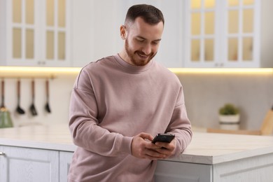 Happy man looking at smartphone in kitchen