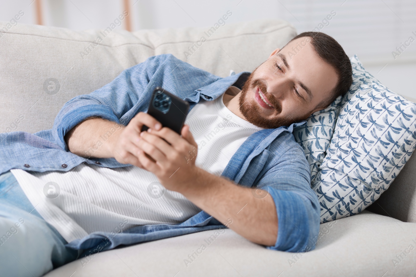 Photo of Smiling man looking at smartphone on sofa