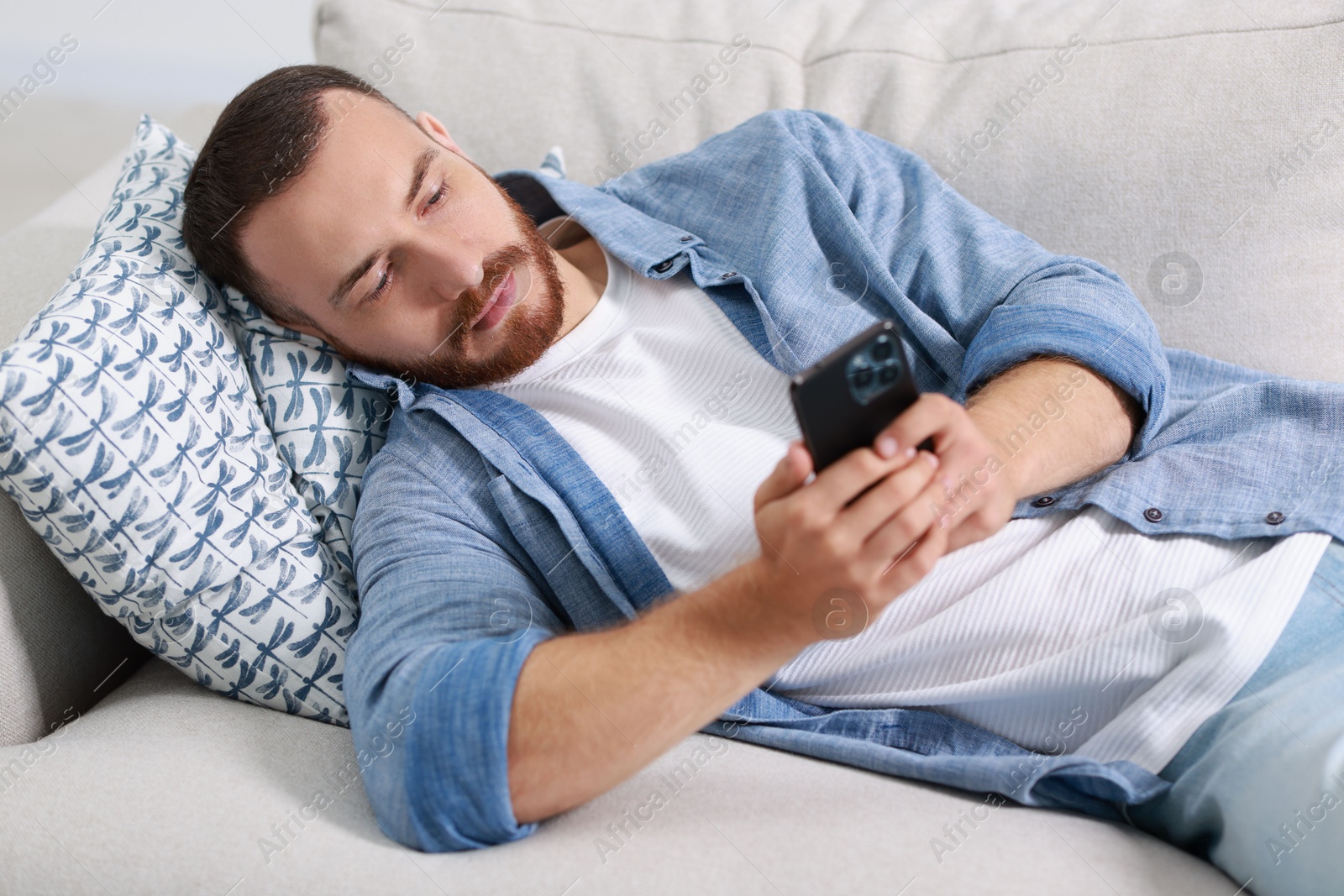 Photo of Handsome man looking at smartphone on sofa