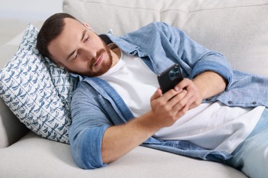 Photo of Handsome man looking at smartphone on sofa