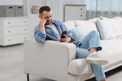 Handsome man using smartphone on sofa indoors