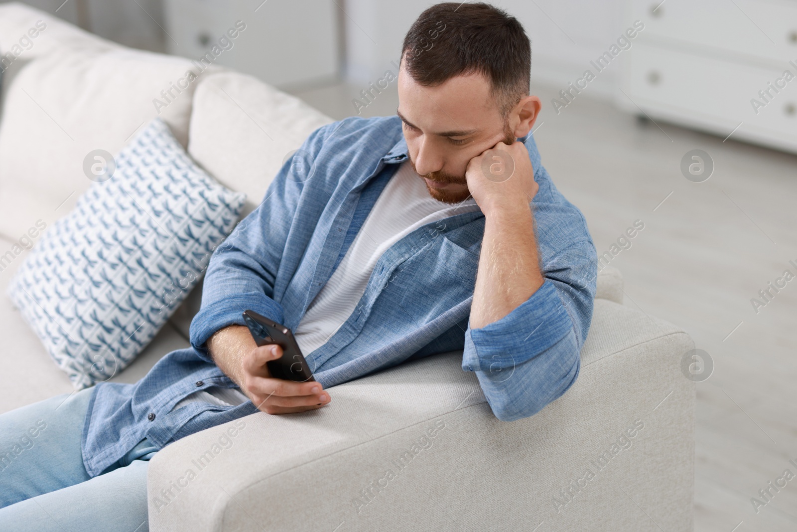 Photo of Handsome man using smartphone on sofa indoors