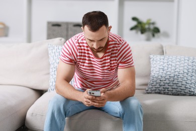 Photo of Handsome man using smartphone on sofa indoors