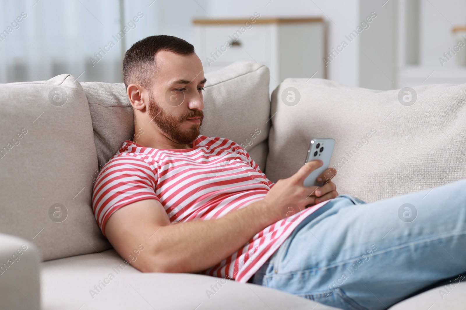 Photo of Handsome man using smartphone on sofa indoors