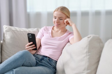 Photo of Smiling woman using smartphone on sofa indoors