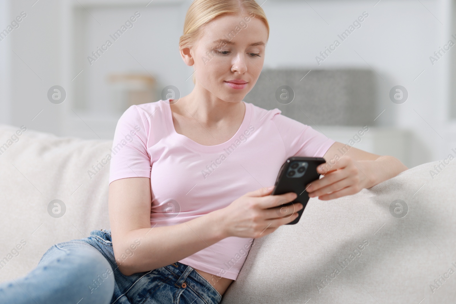 Photo of Beautiful woman using smartphone on sofa indoors