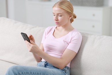 Photo of Beautiful woman using smartphone on sofa indoors