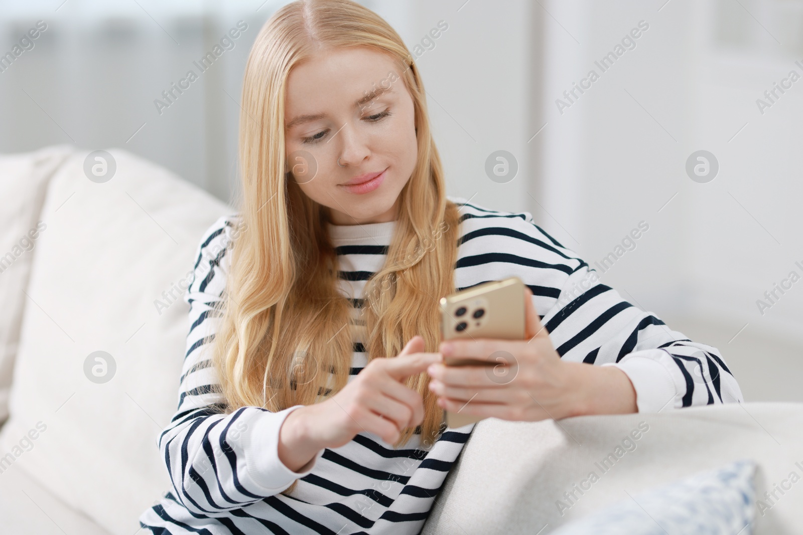 Photo of Beautiful woman using smartphone on sofa indoors