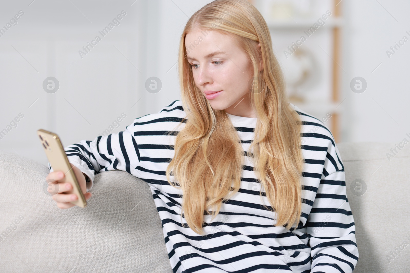 Photo of Beautiful woman using smartphone on sofa indoors