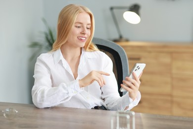 Photo of Smiling woman using smartphone at table in office