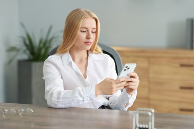 Photo of Beautiful woman using smartphone at table in office