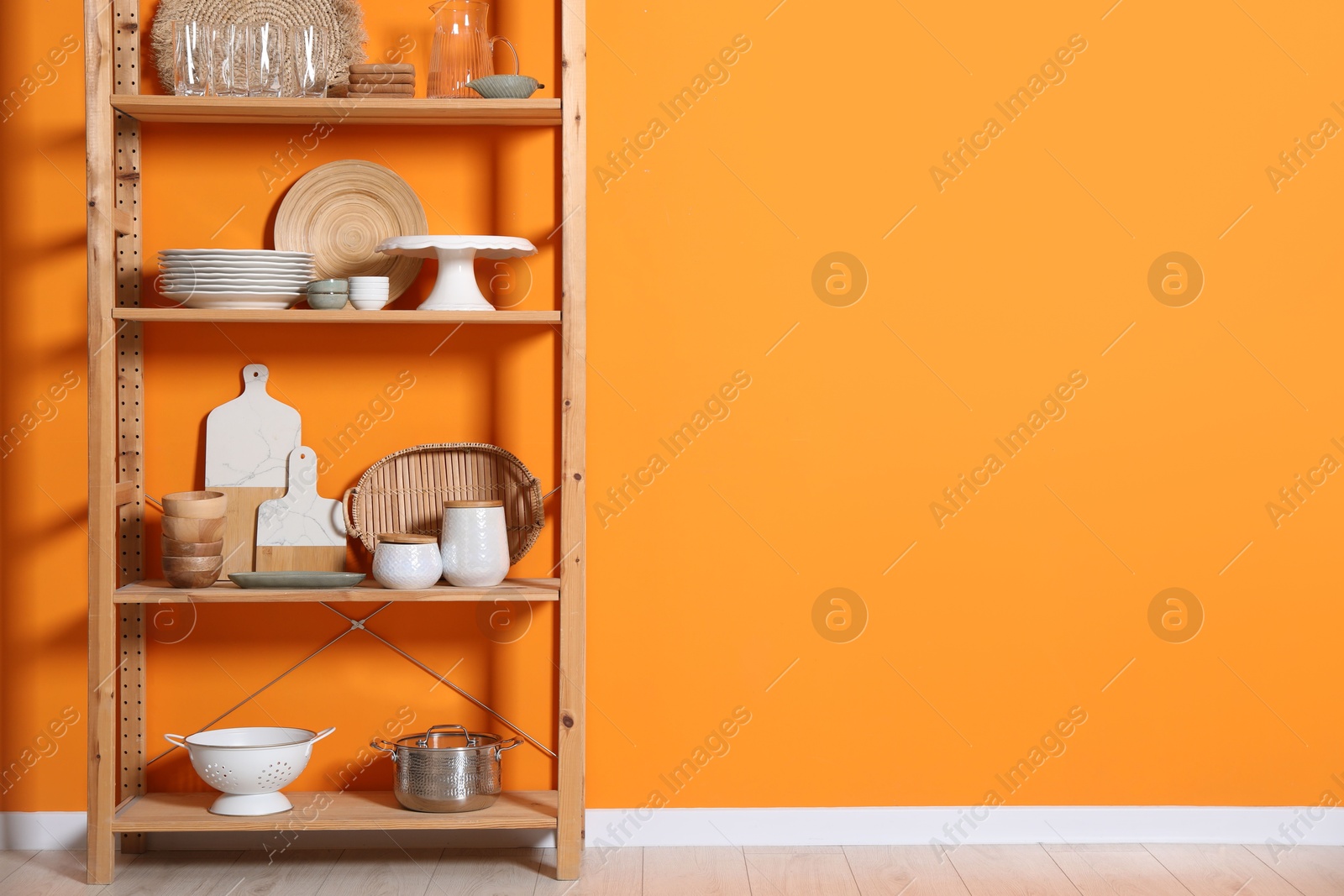 Photo of Wooden storage stand with kitchenware near orange wall indoors, space for text