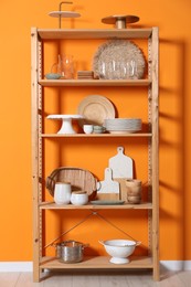 Wooden storage stand with kitchenware near orange wall indoors