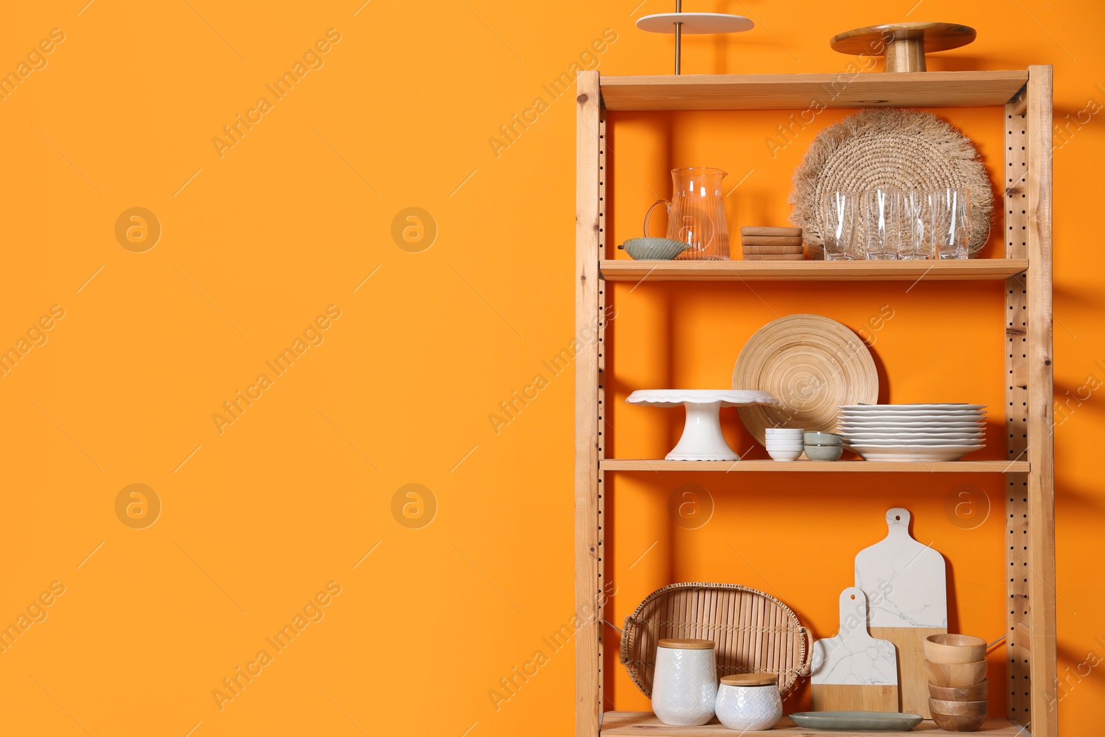 Photo of Wooden storage stand with kitchenware near orange wall indoors, space for text