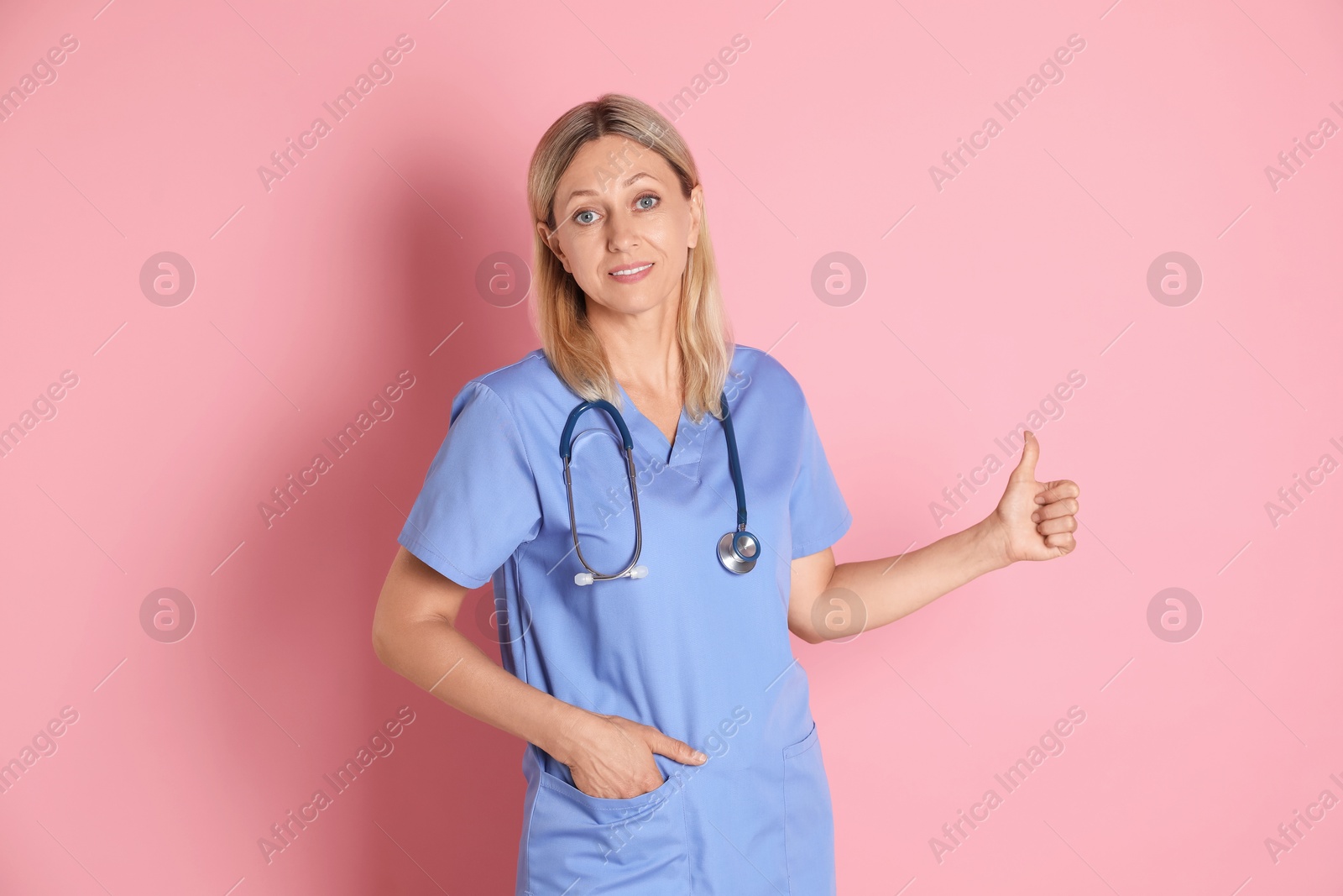 Photo of Doctor in medical uniform with stethoscope showing thumbs up on pink background