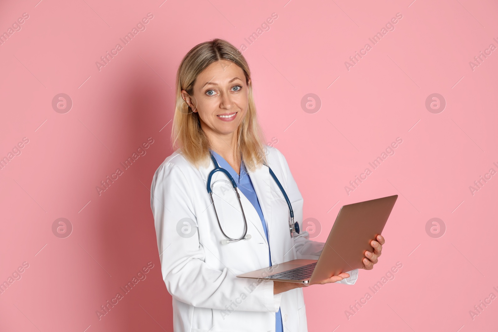 Photo of Doctor in medical uniform with stethoscope and laptop on pink background