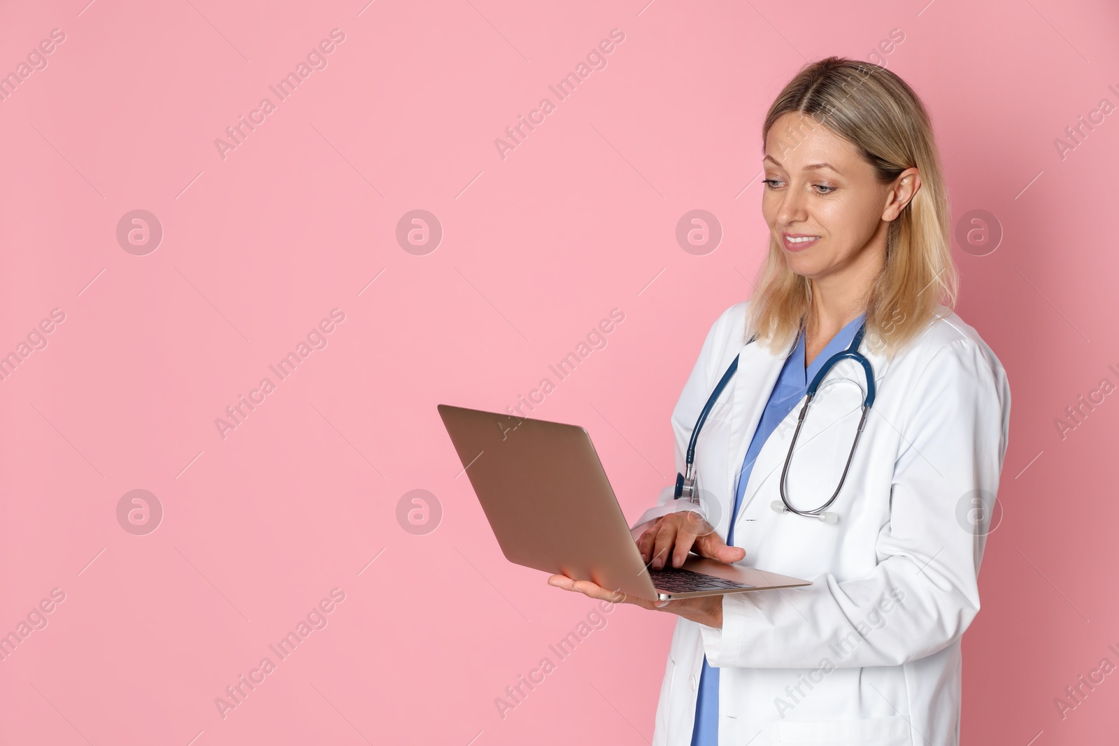 Photo of Doctor in medical uniform with stethoscope and laptop on pink background, space for text