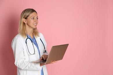 Photo of Doctor in medical uniform with stethoscope and laptop on pink background, space for text