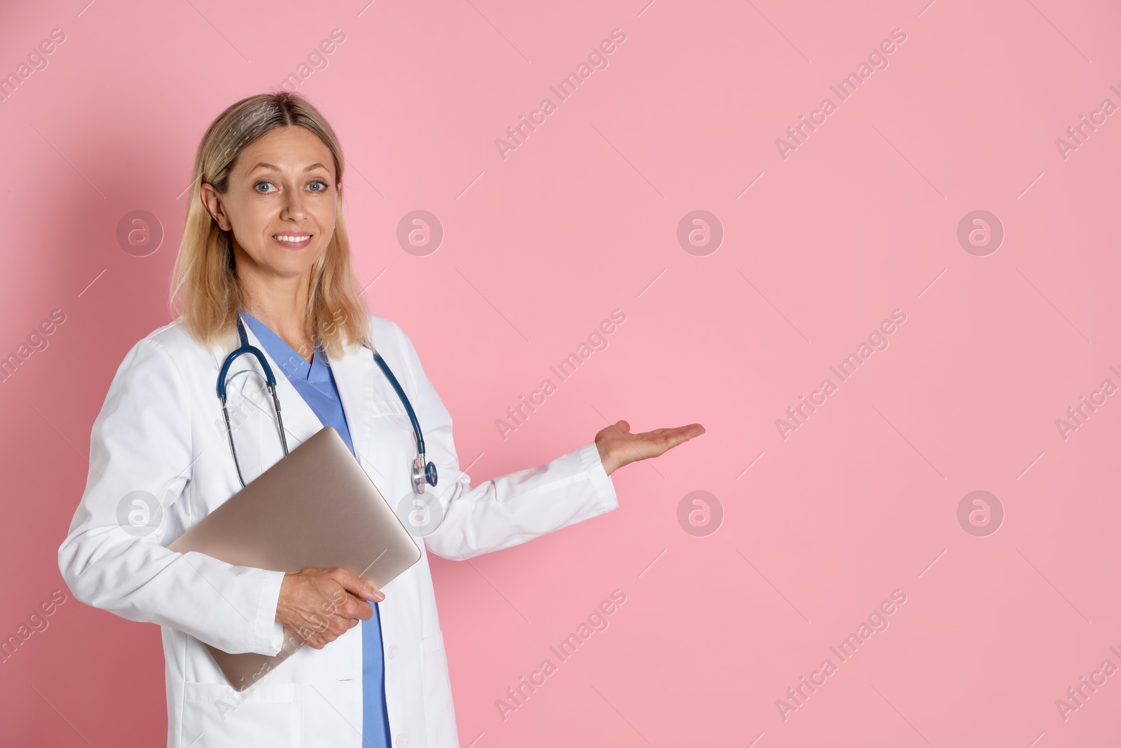 Photo of Doctor in medical uniform with stethoscope and laptop on pink background, space for text