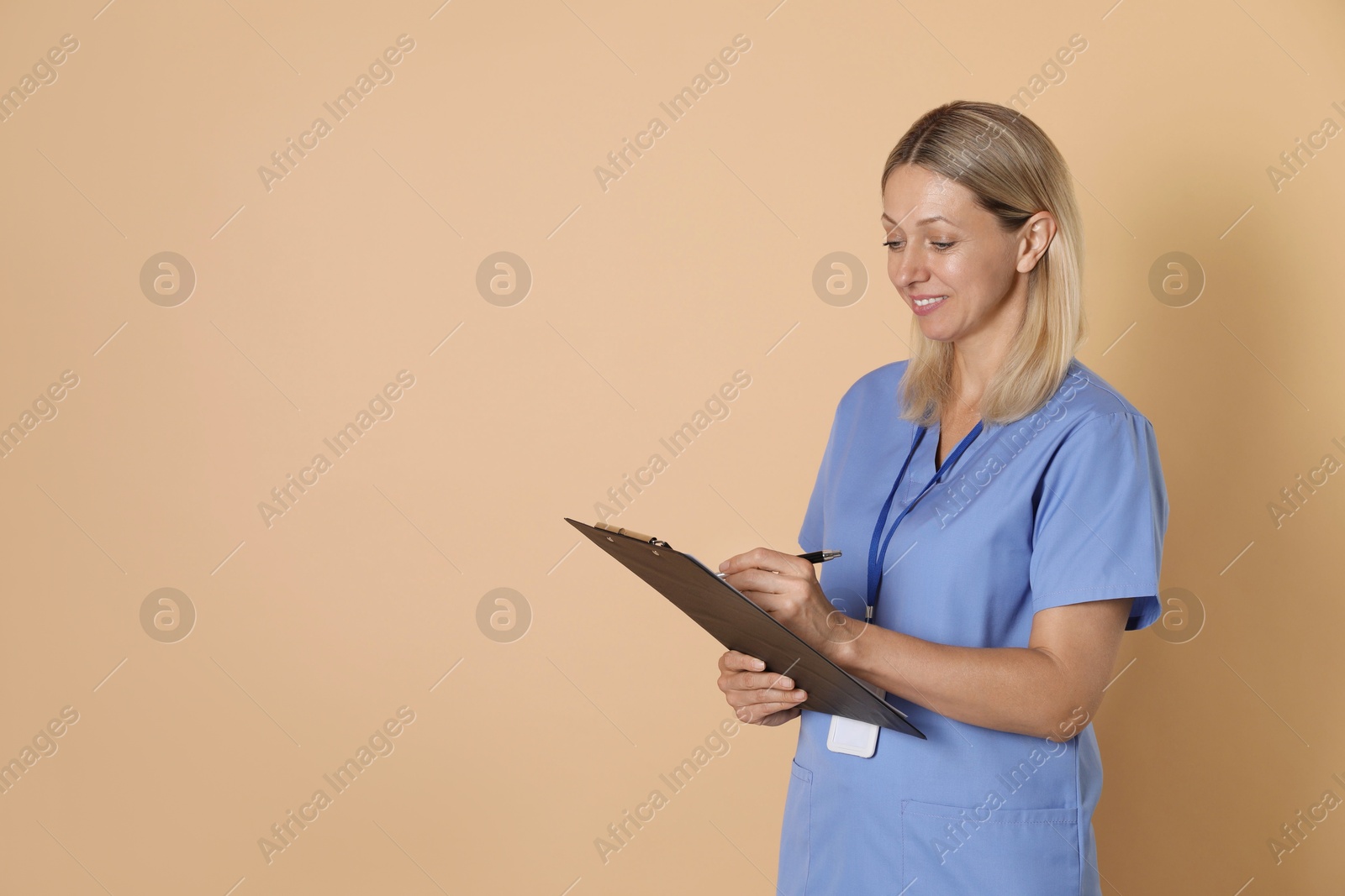 Photo of Nurse in medical uniform with badge and clipboard on beige background, space for text