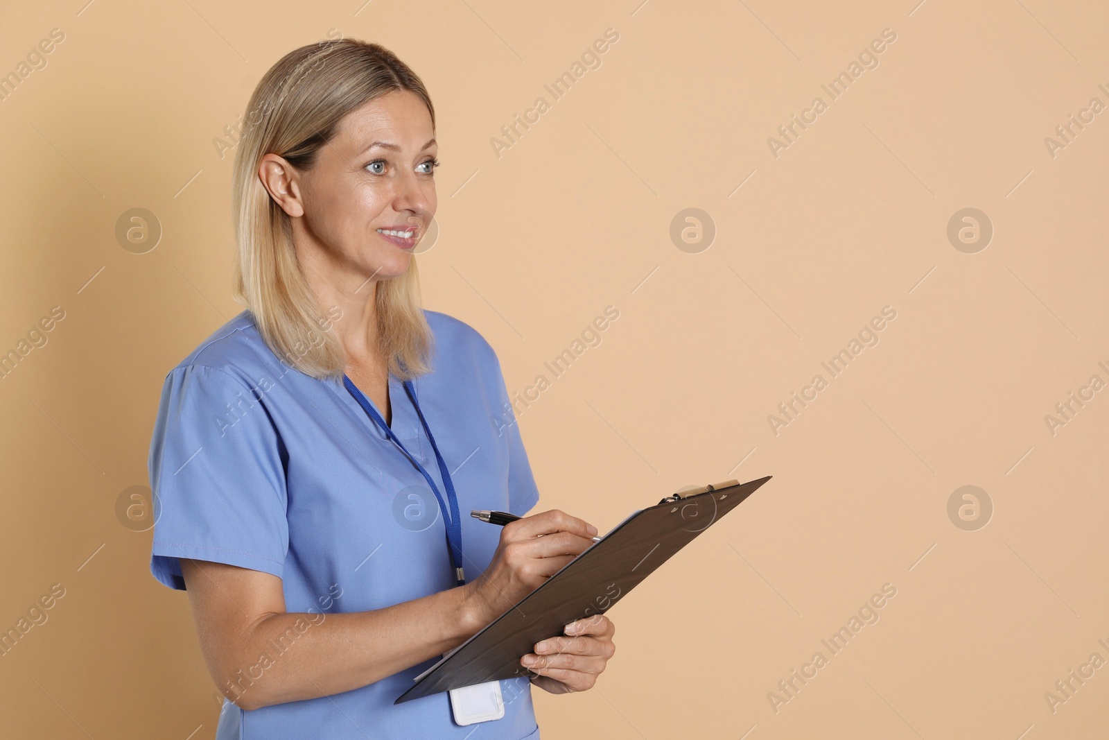 Photo of Nurse in medical uniform with badge and clipboard on beige background