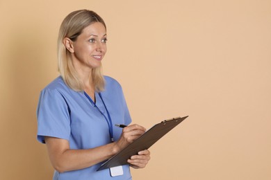 Photo of Nurse in medical uniform with badge and clipboard on beige background