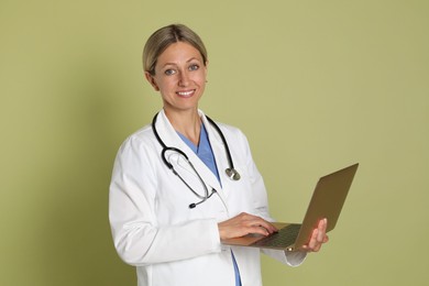 Doctor in medical uniform with stethoscope and laptop on light green background