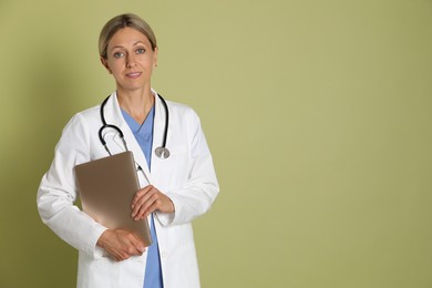 Doctor in medical uniform with stethoscope and laptop on light green background, space for text