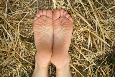 Photo of Woman lying barefoot on straw outdoors, top view