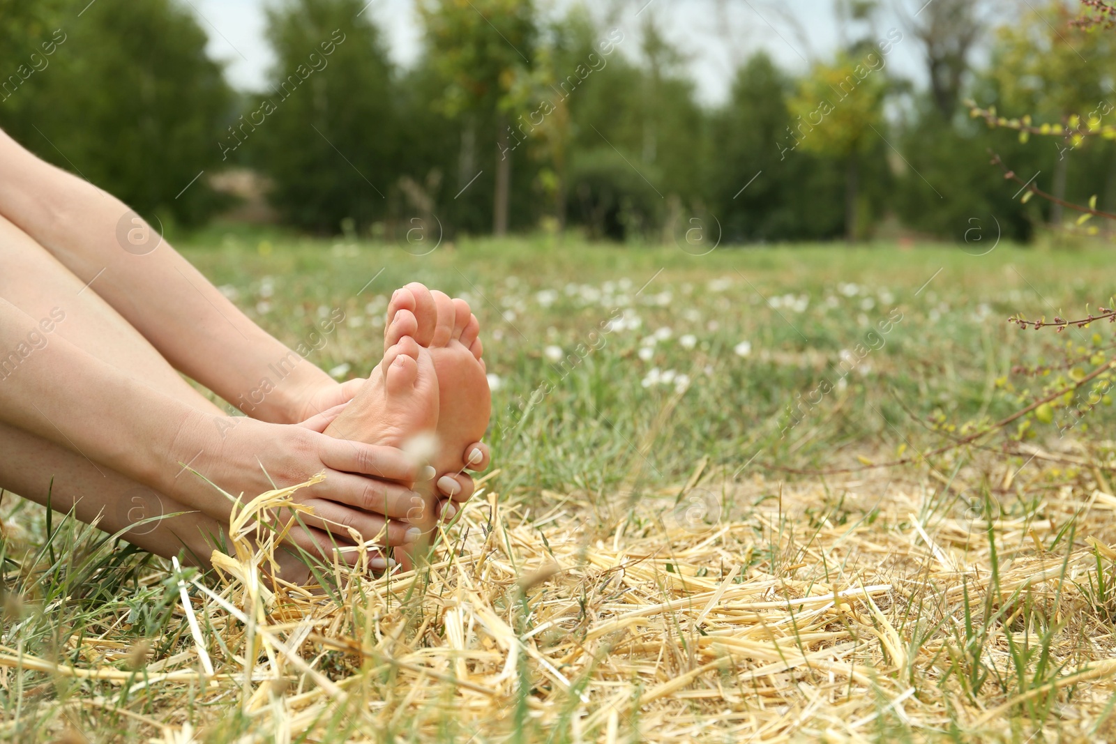 Photo of Woman sitting barefoot on straw outdoors, closeup. Space for text