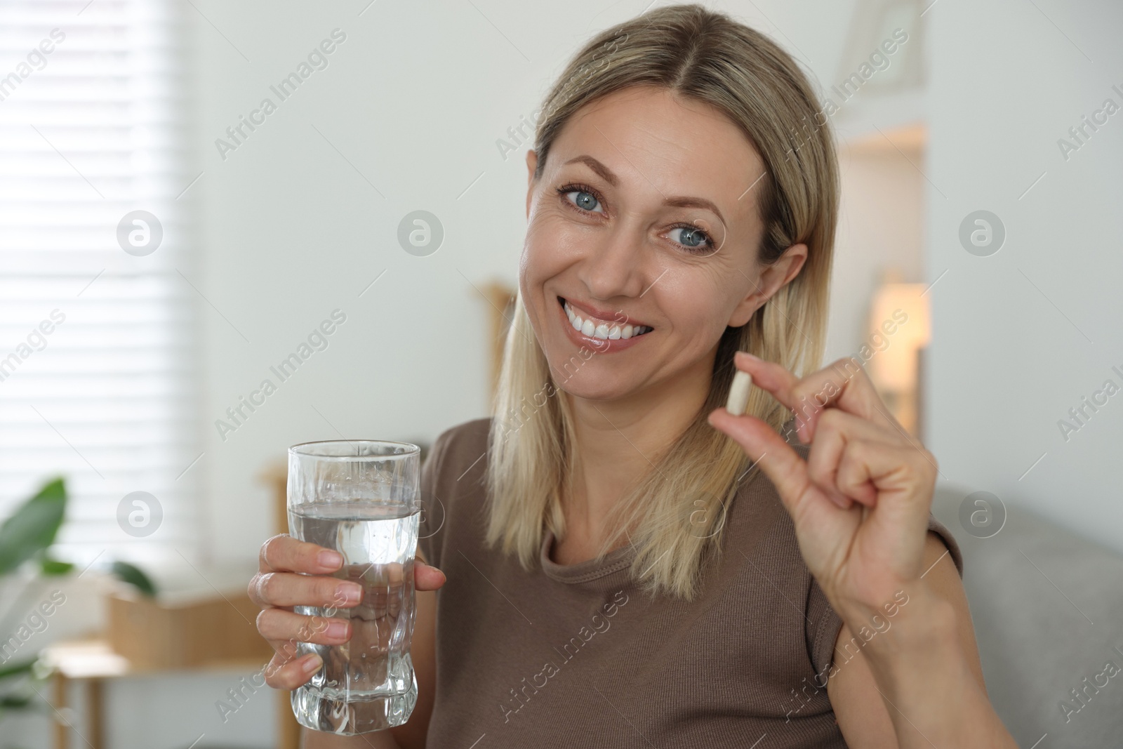 Photo of Menopause, hormone replacement therapy. Happy woman with glass of water and pill at home