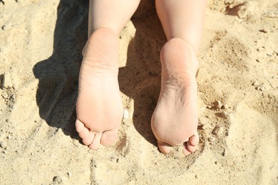 Photo of Woman lying barefoot on sand outdoors, closeup