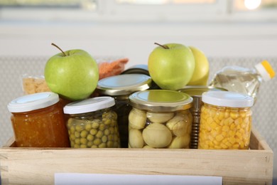 Photo of Different food products for donation in wooden crate indoors, closeup