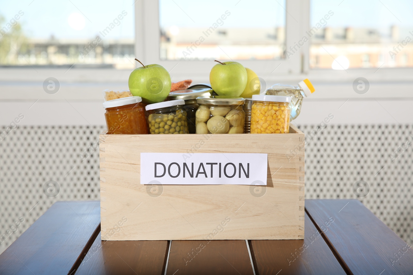 Photo of Different food products for donation in wooden crate on table indoors