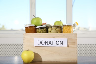 Photo of Different food products for donation in wooden crate on table indoors