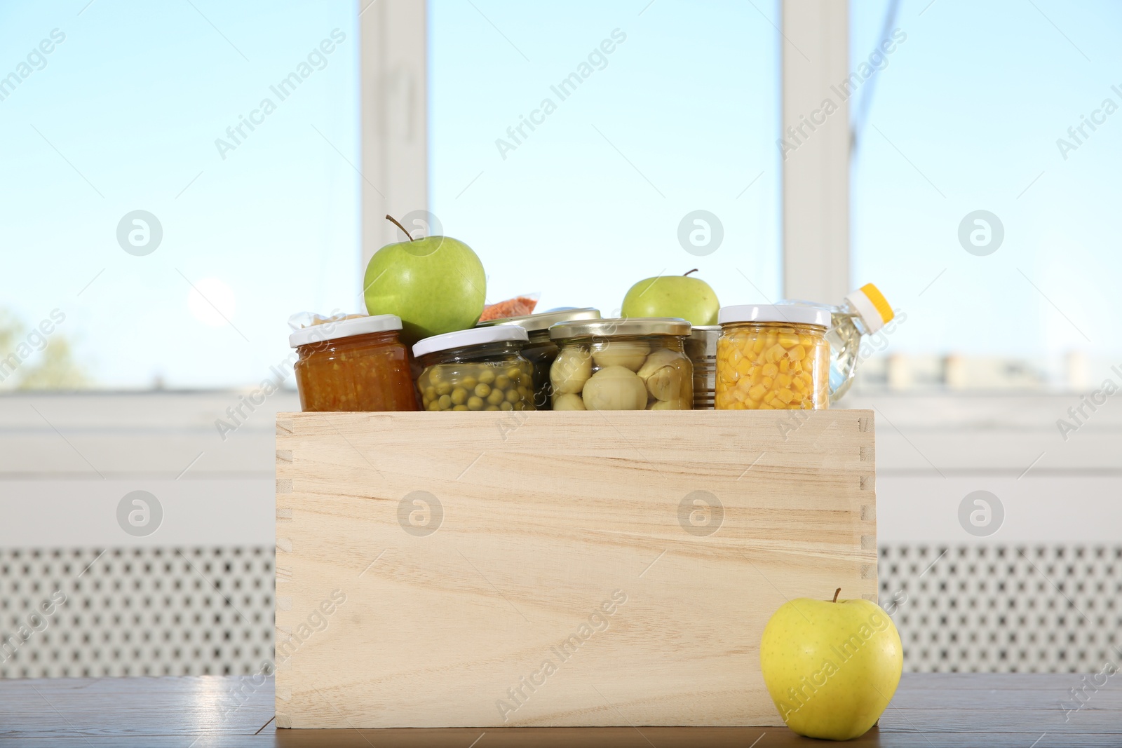 Photo of Different food products for donation in wooden crate on table indoors