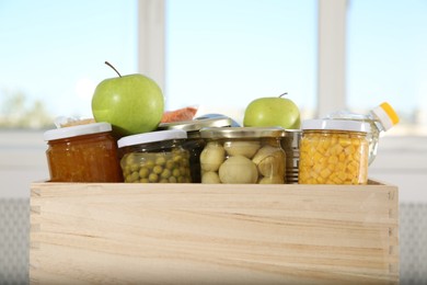 Photo of Different food products for donation in wooden crate indoors, closeup