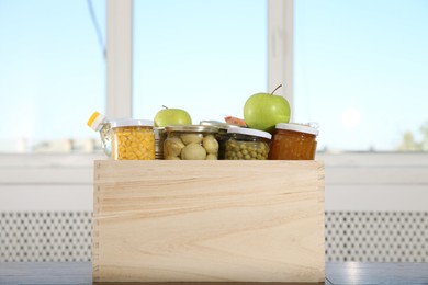 Photo of Different food products for donation in wooden crate on table indoors