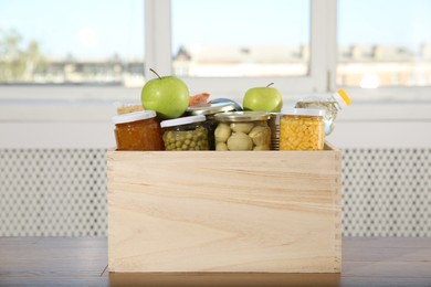 Photo of Different food products for donation in wooden crate on table indoors